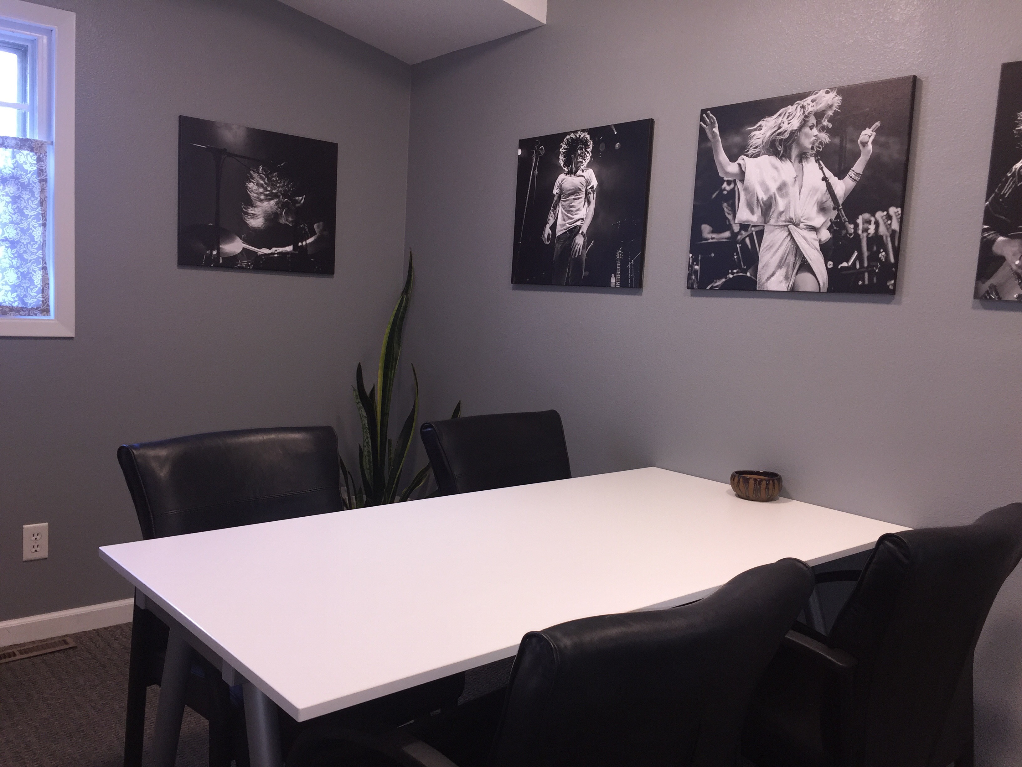 Image of the room setup with a table, 4 chairs and shows the photographs of musicians, a plant and a window.